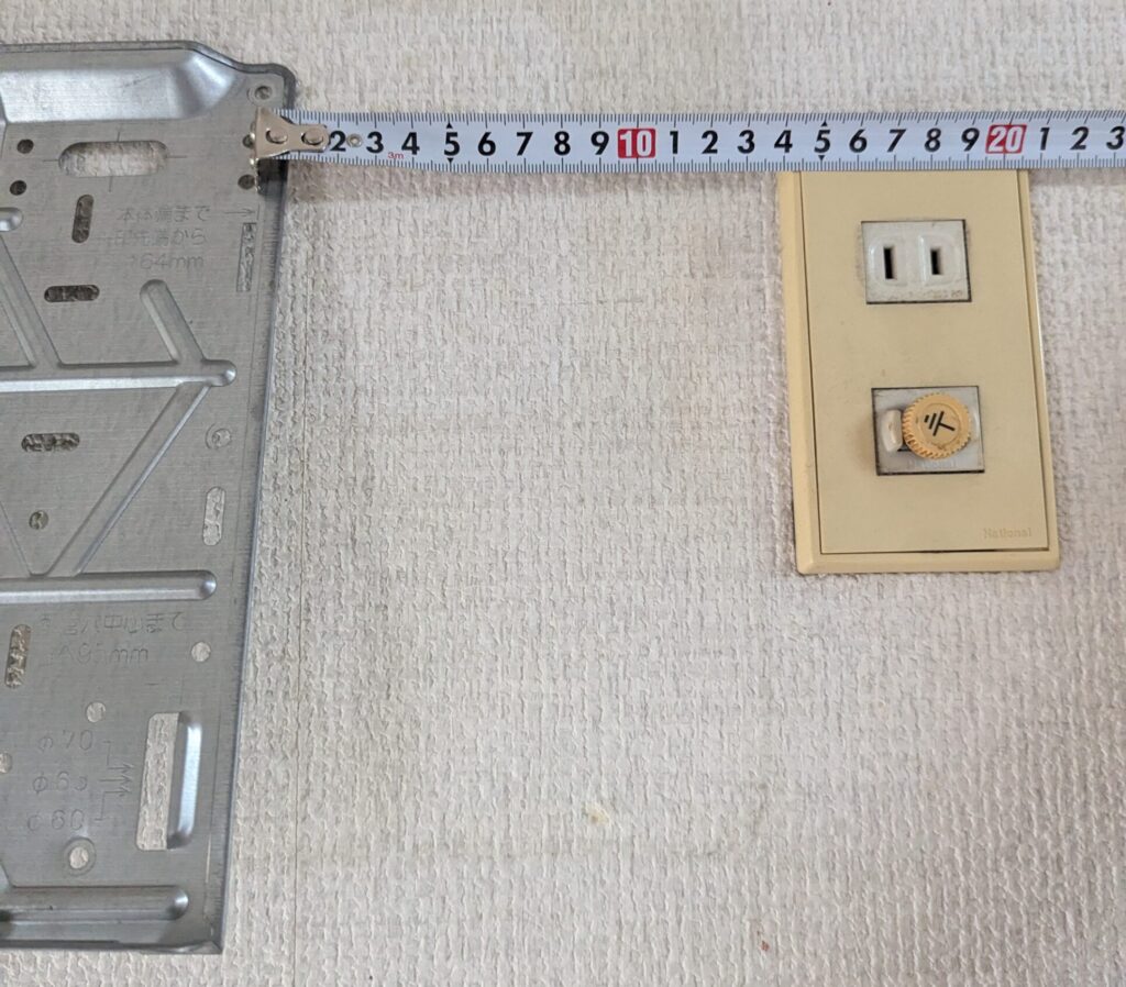 据付板の右端から既存の電源コンセント穴までの距離をメジャーで測定している様子