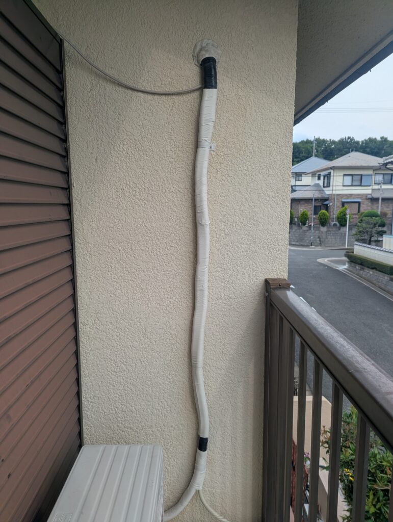 外壁に沿って非粘着テープとサドルで固定され、壁穴がパテ埋めされたエアコン配管